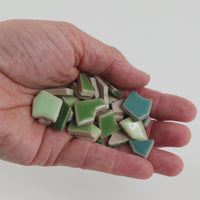 Video of Flip ceramic puzzle pieces in green mix, opaque glazed porcelain, 4–20 mm, held in a hand and poured out to show their shapes and finish