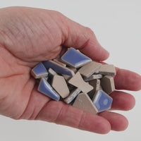 Video of Flip ceramic puzzle pieces in foxglove, opaque glazed porcelain, 4–20 mm, held in a hand and poured out to show their shapes and finish