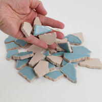 Video of Flip XL ceramic puzzle pieces in ice blue, opaque glazed porcelain, 20–60 mm, picked up from a pile by hand and dropped back to show their size, shapes and finish