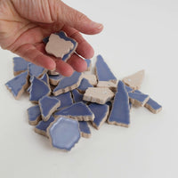 Video of Flip XL ceramic puzzle pieces in foxglove, opaque glazed porcelain, 20–60 mm, picked up from a pile by hand and dropped back to show their size, shapes and finish