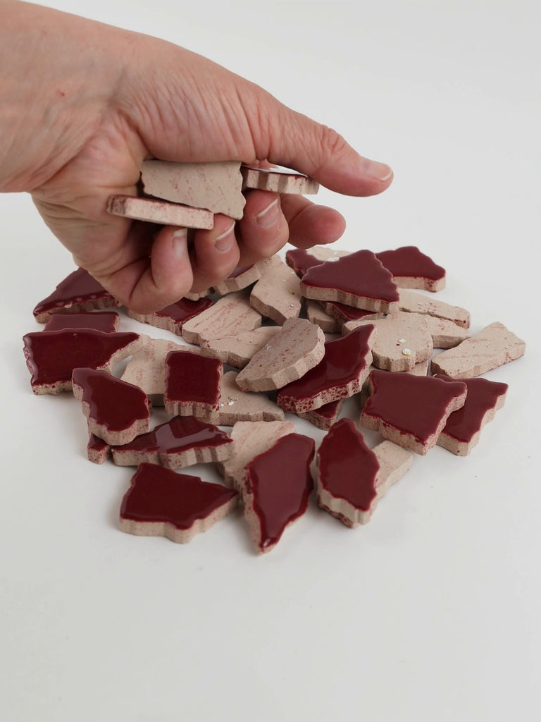 Video of Flip XL ceramic puzzle pieces in old pink, opaque glazed porcelain, 20–60 mm, picked up from a pile by hand and dropped back to show their size, shapes and finish