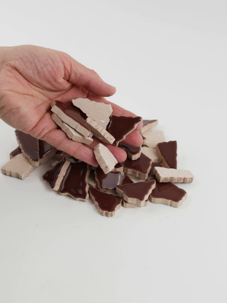 Video of Flip XL ceramic puzzle pieces in mocha, opaque glazed porcelain, 20–60 mm, picked up from a pile by hand and dropped back to show their size, shapes and finish