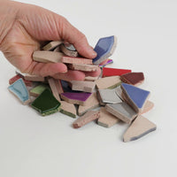 Video of Flip XL ceramic puzzle pieces in tropical mix, opaque glazed porcelain, 20–60 mm, picked up from a pile by hand and dropped back to show their size, shapes and finish