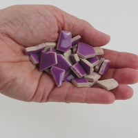 Video of Flip ceramic puzzle pieces in purple, opaque glazed porcelain, 4–20 mm, held in a hand and poured out to show their shapes and finish