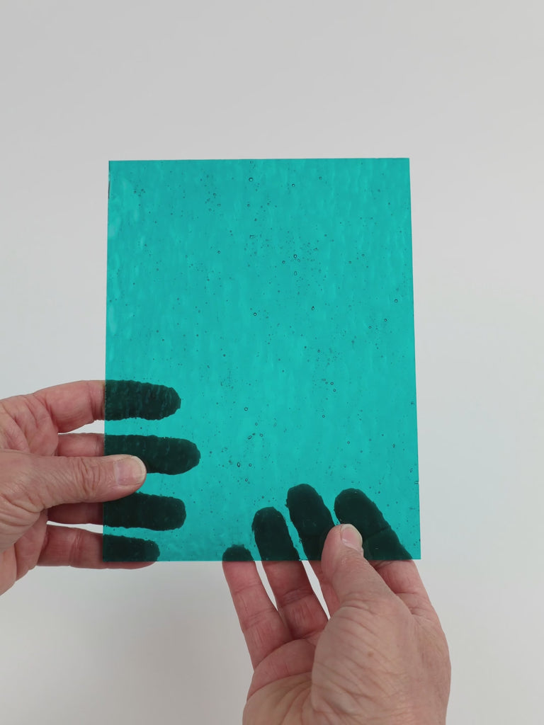 Video of the Dark Turquoise Hammered glass plate in hammered transparent turquoise, 15x19cm, held up and tilted to show its pattern and transparency